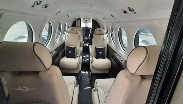 The aircraft cabin features light-colored leather seats arranged in a club configuration with large windows.
