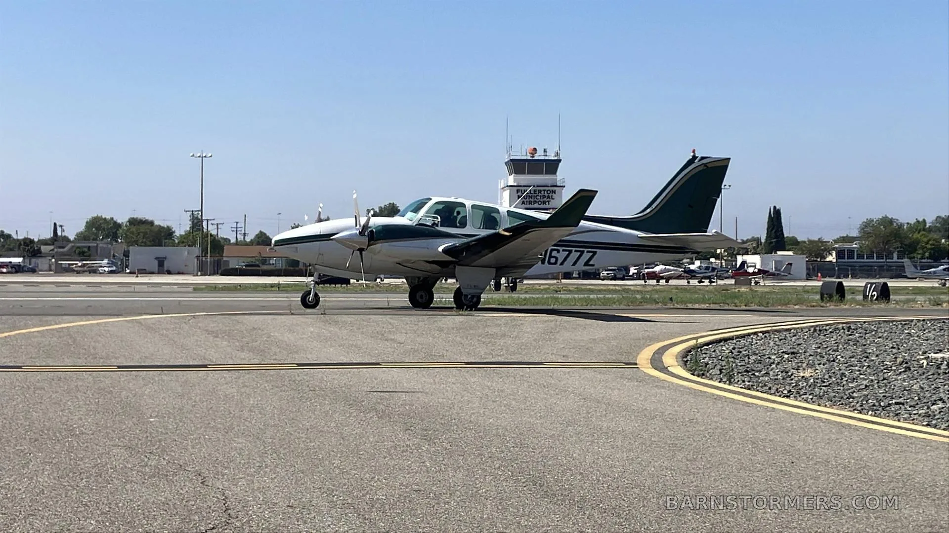 A white and green twin-engine propeller aircraft (N677Z) on a taxiway with an airport control tower in the background.