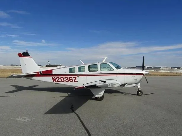 Side view of a white Beechcraft Bonanza N2036Z with red and black stripes on an airport tarmac.