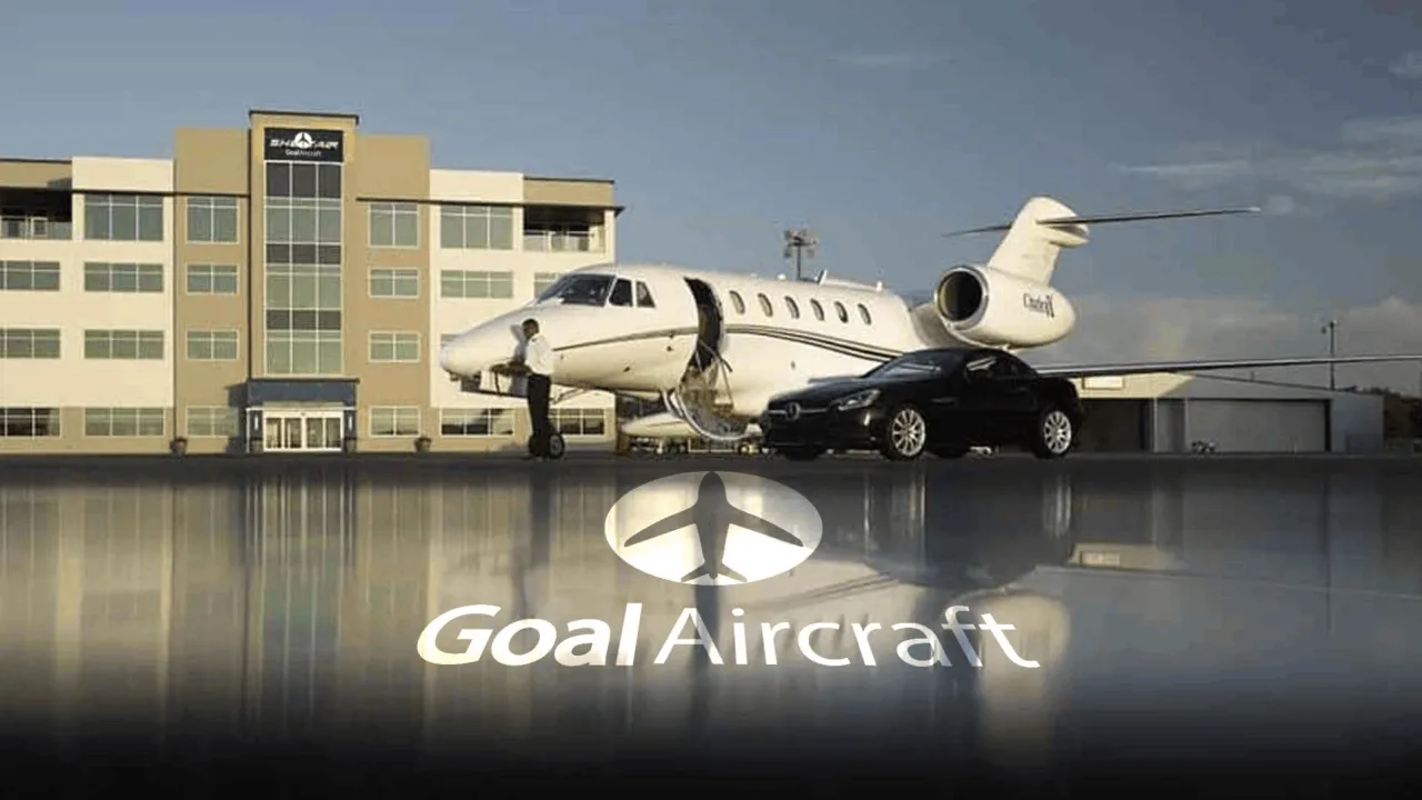 A white Cessna Citation business jet with a dark stripe is parked on a tarmac next to a black car and a person, in front of a modern building.