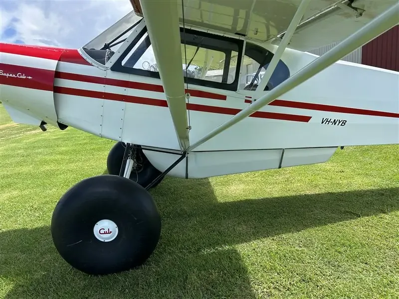 A close-up side view of the white and red Super Cub showing the VH-NYB registration and a large tundra tire.