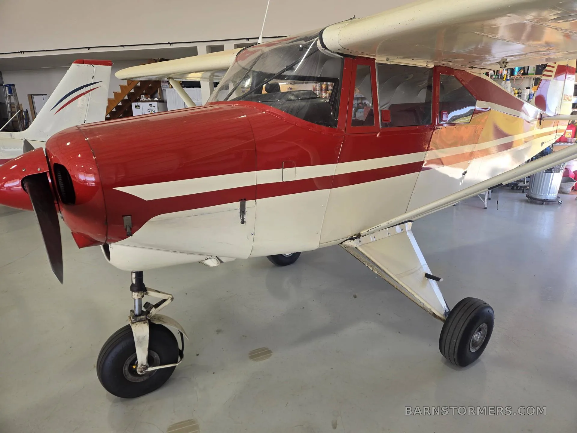 A red and white single-engine propeller aircraft with tricycle landing gear, parked in a hangar.