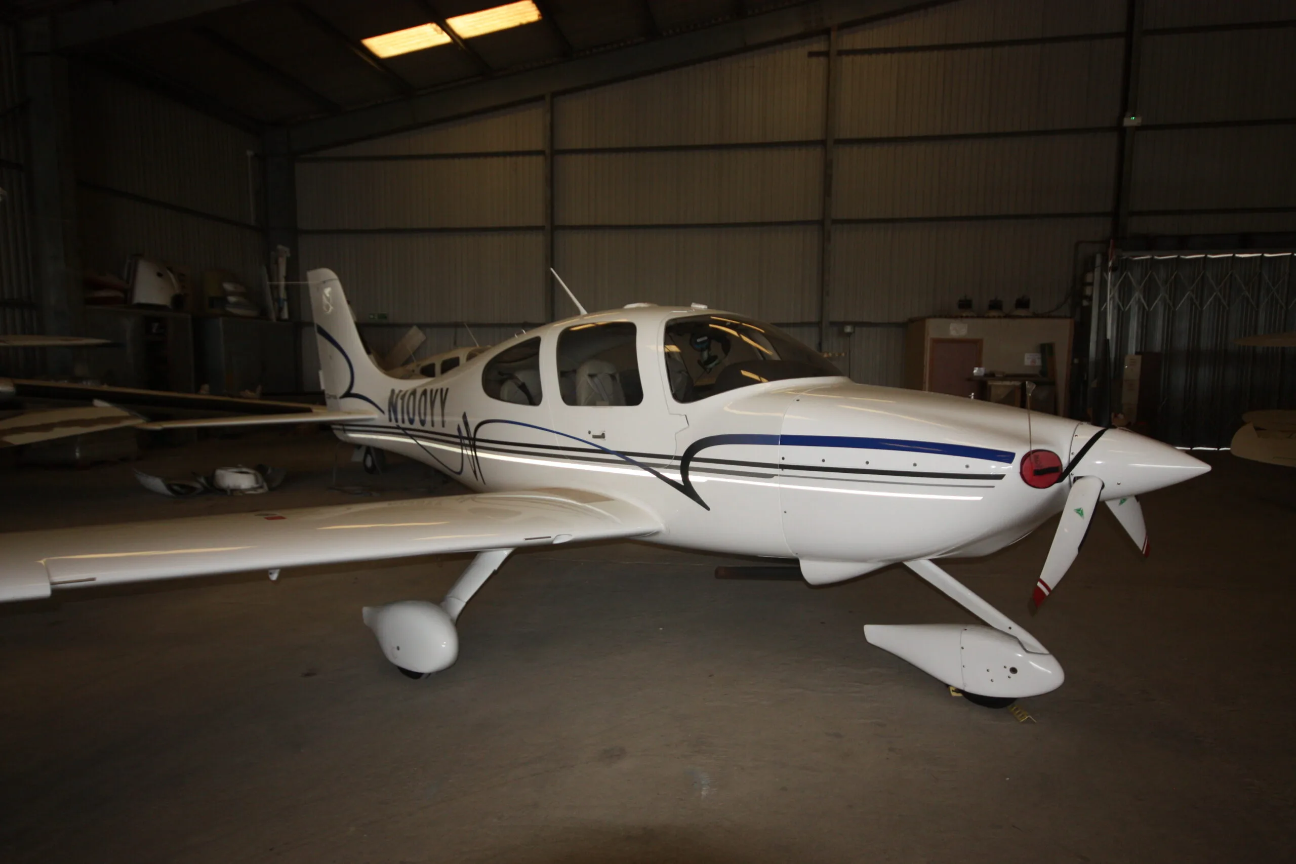 A white Cirrus SR22 aircraft with blue and grey stripes parked inside a hangar.