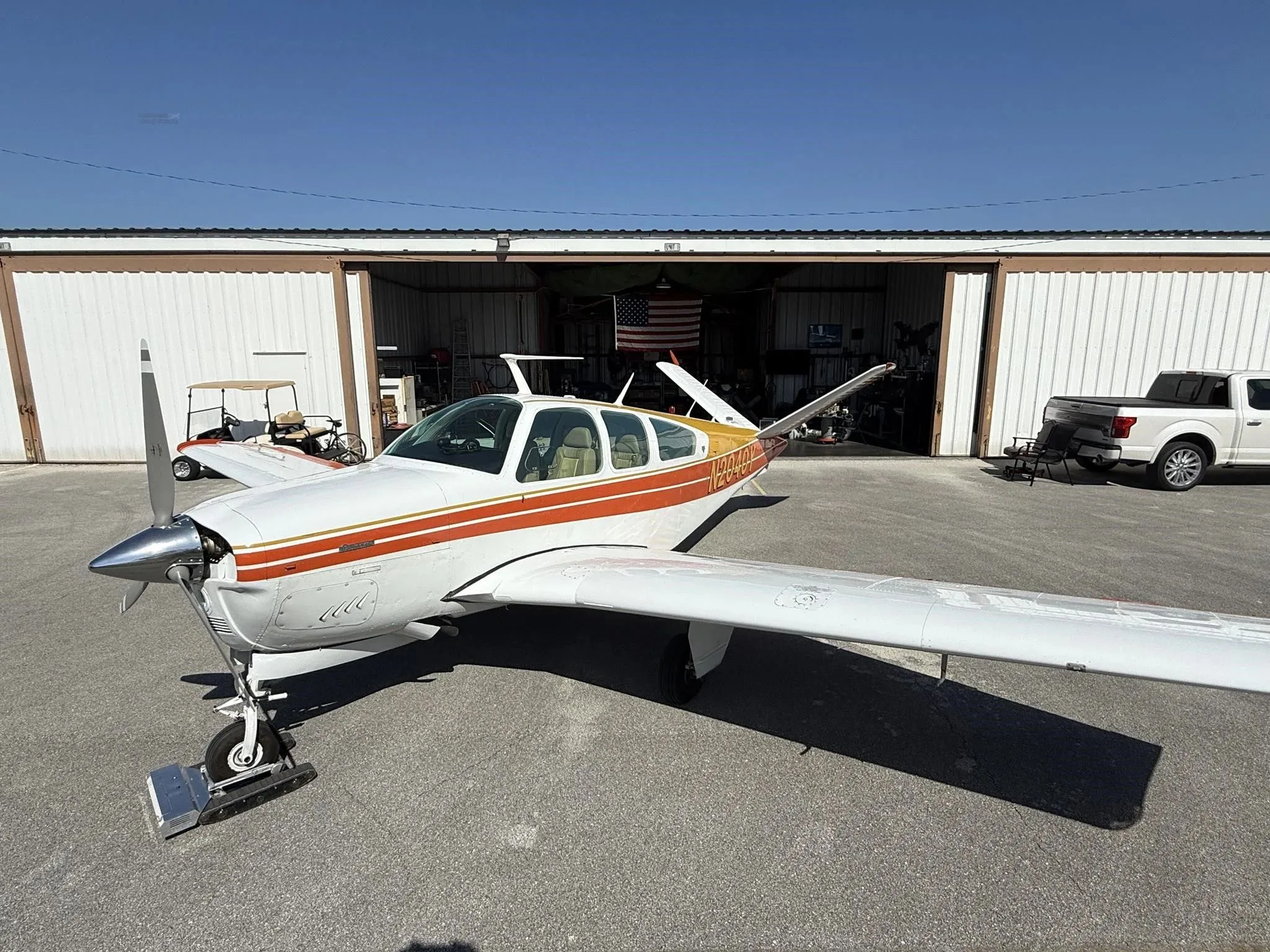 A white and orange single-engine aircraft, N2040Y, parked on an asphalt ramp in front of a hangar.