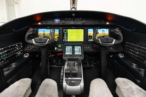 The modern cockpit features multiple digital displays, yokes, and a central control panel.
