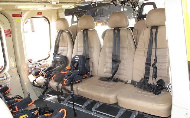 A closer view of the helicopter's interior cabin shows beige seats equipped with black and orange safety harnesses.