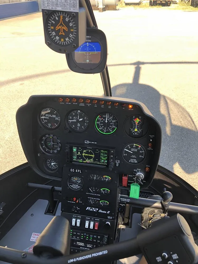 The cockpit of a Robinson R22 Beta II helicopter, showing the instrument panel with analog gauges and a Garmin display.