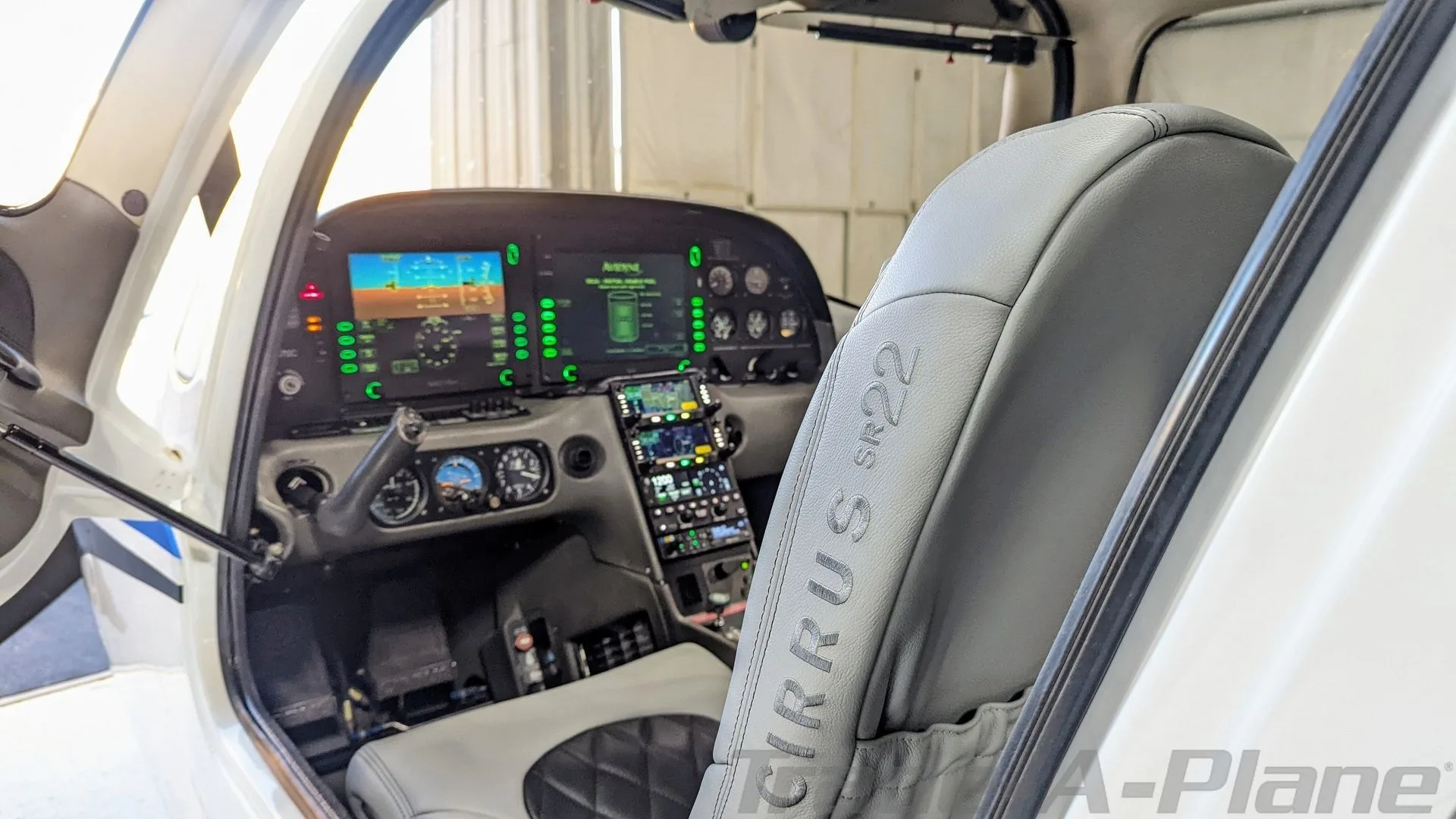 View from the cabin into the cockpit of a Cirrus SR22, showing the instrument panel and a grey seat with "CIRRUS SR22" embossed.