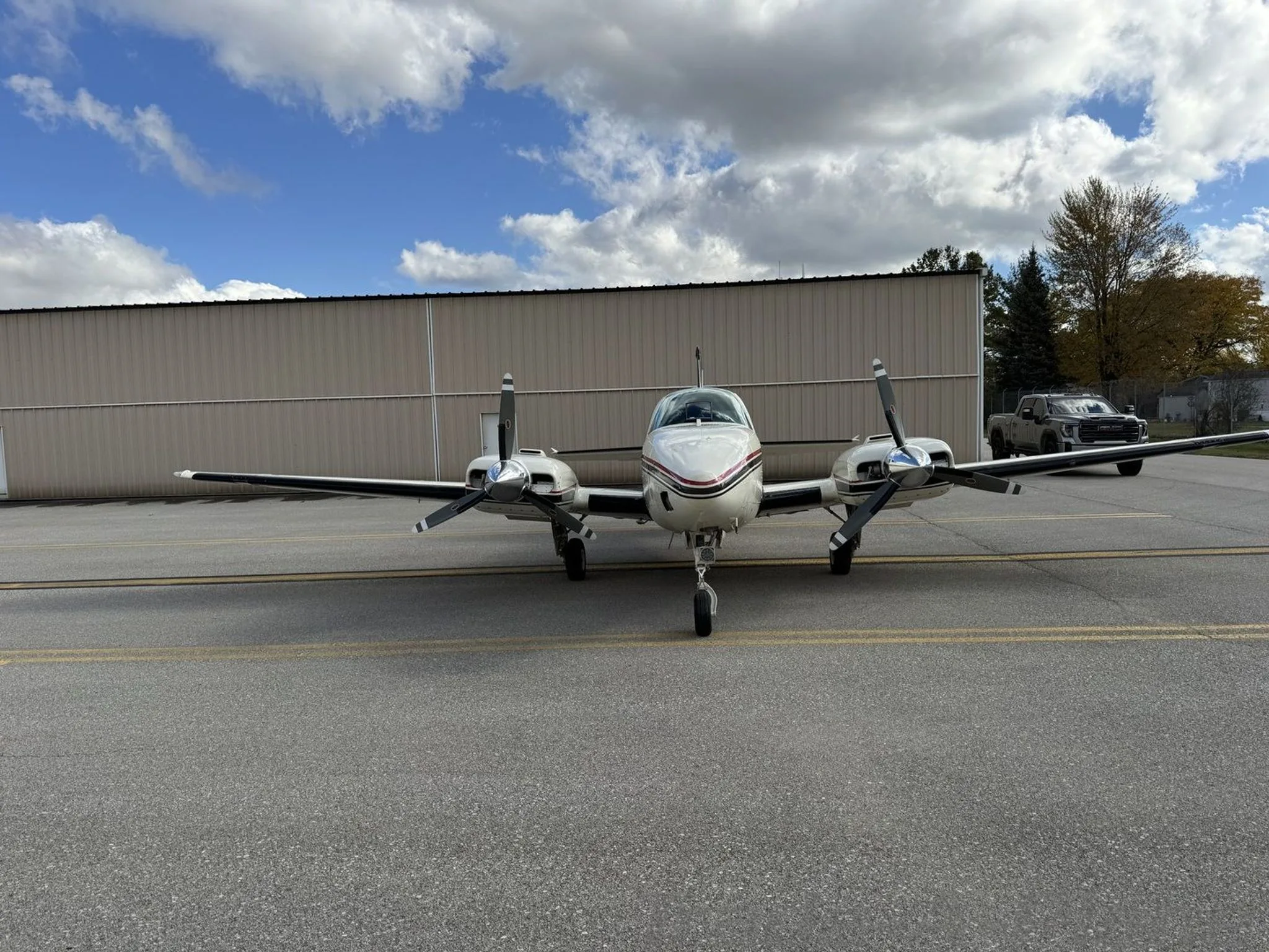 A head-on view of the N185A twin-engine aircraft, white with red and black stripes, parked on an airport tarmac.