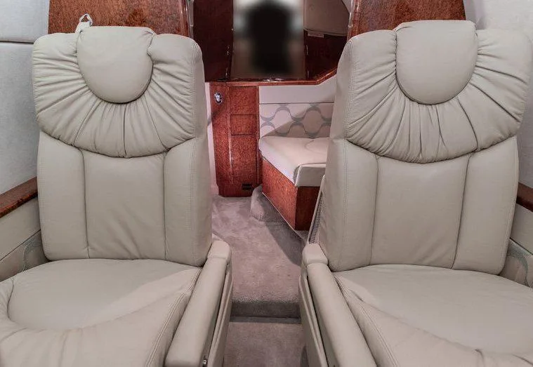 The rear interior cabin of a private jet, showing beige leather seats, wood paneling, and a divan.
