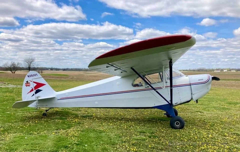 A white and red Piper Cub-style aircraft with registration N35001 parked in a grassy field under a cloudy sky.