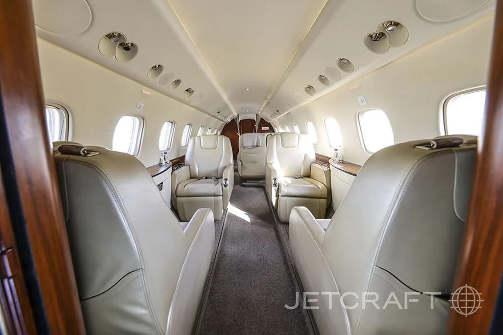 The aircraft cabin features light-colored leather seats in a 1-1 configuration with a central aisle.