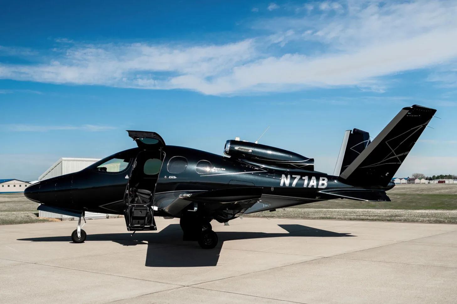 A black Cirrus Vision Jet (N71AB) with a grey underside and geometric tail design, parked on an airport tarmac with its main door open.