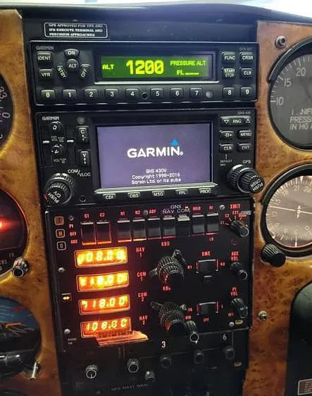 A close-up of the aircraft's avionics stack, featuring a Garmin GNS 430V and other navigation radios on a wood grain panel.