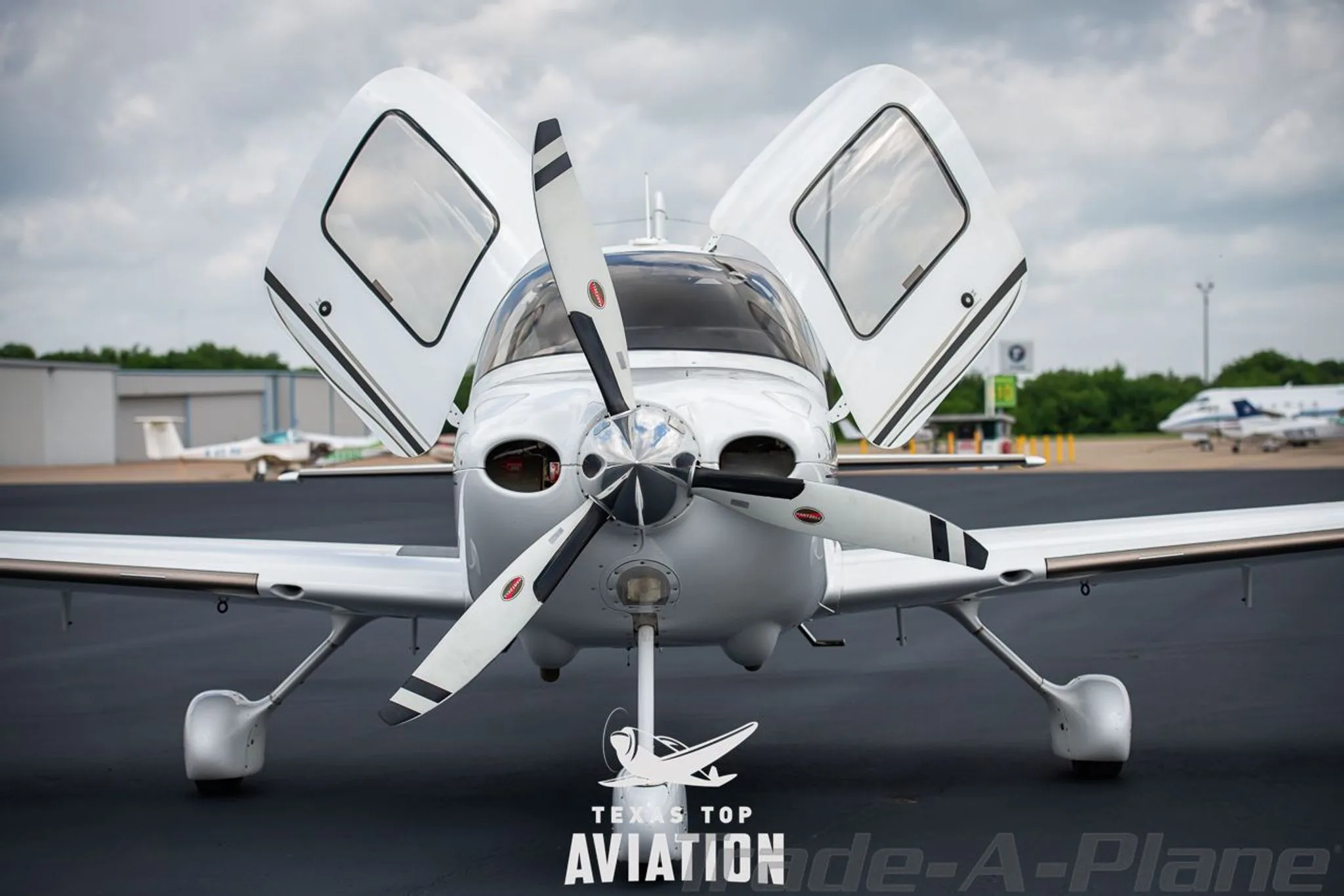 A front view of a white Cirrus SR22 aircraft, registration N173SR, parked on an airfield with its gull-wing doors open.