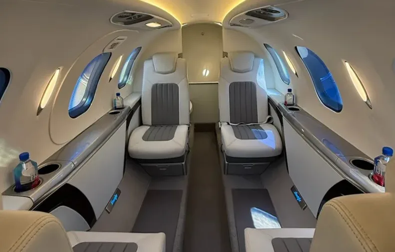 The luxurious interior cabin of a HondaJet HA-420, showing two rows of white and grey leather seats with water bottles on side tables.