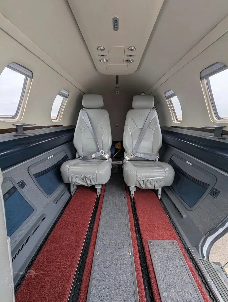 The interior cabin of an Eclipse jet, showing two grey leather seats facing forward with red and grey carpet.