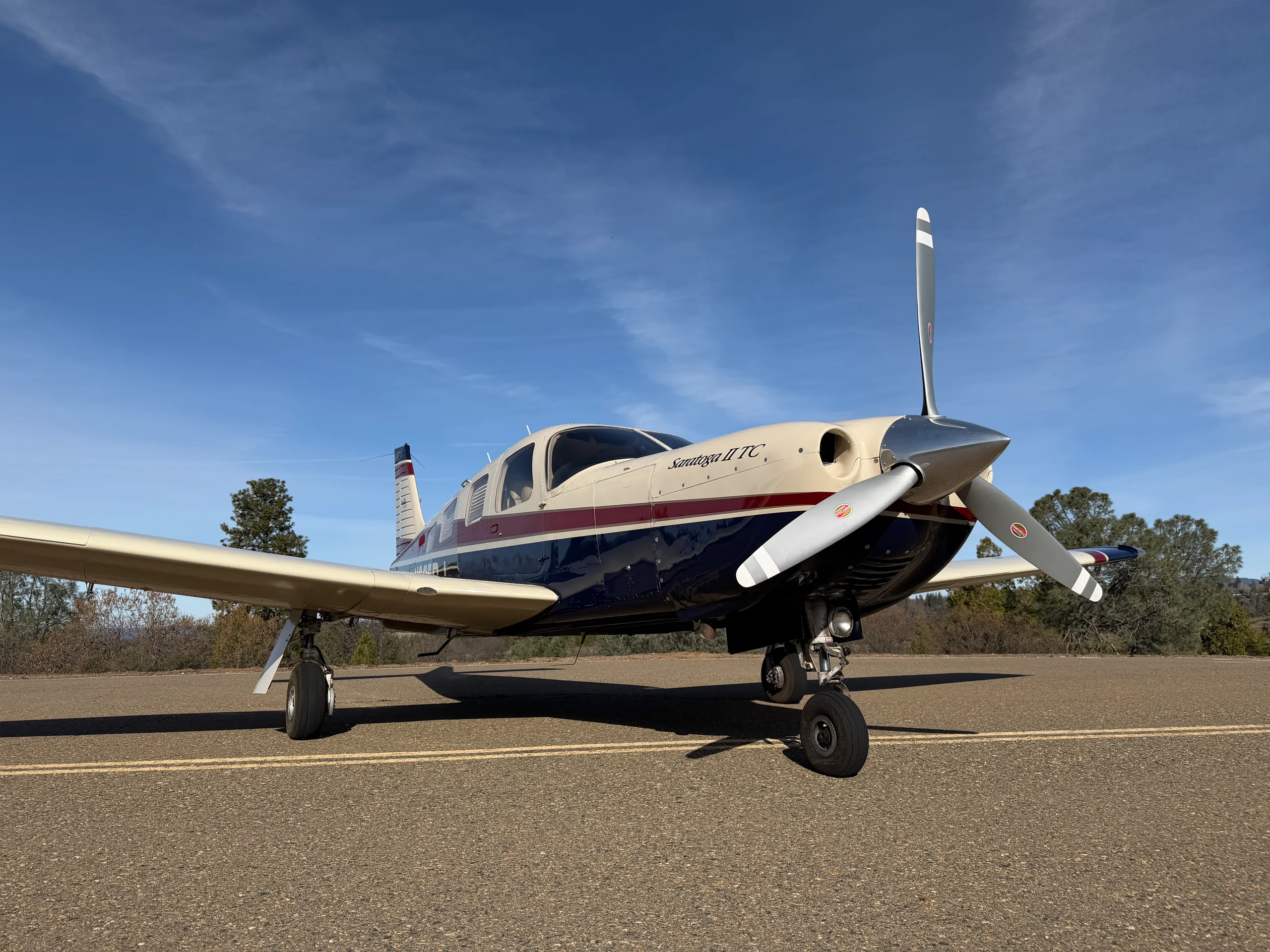 A low-angle front-side view of the Piper Saratoga II TC aircraft with a cream, blue, and red paint scheme.