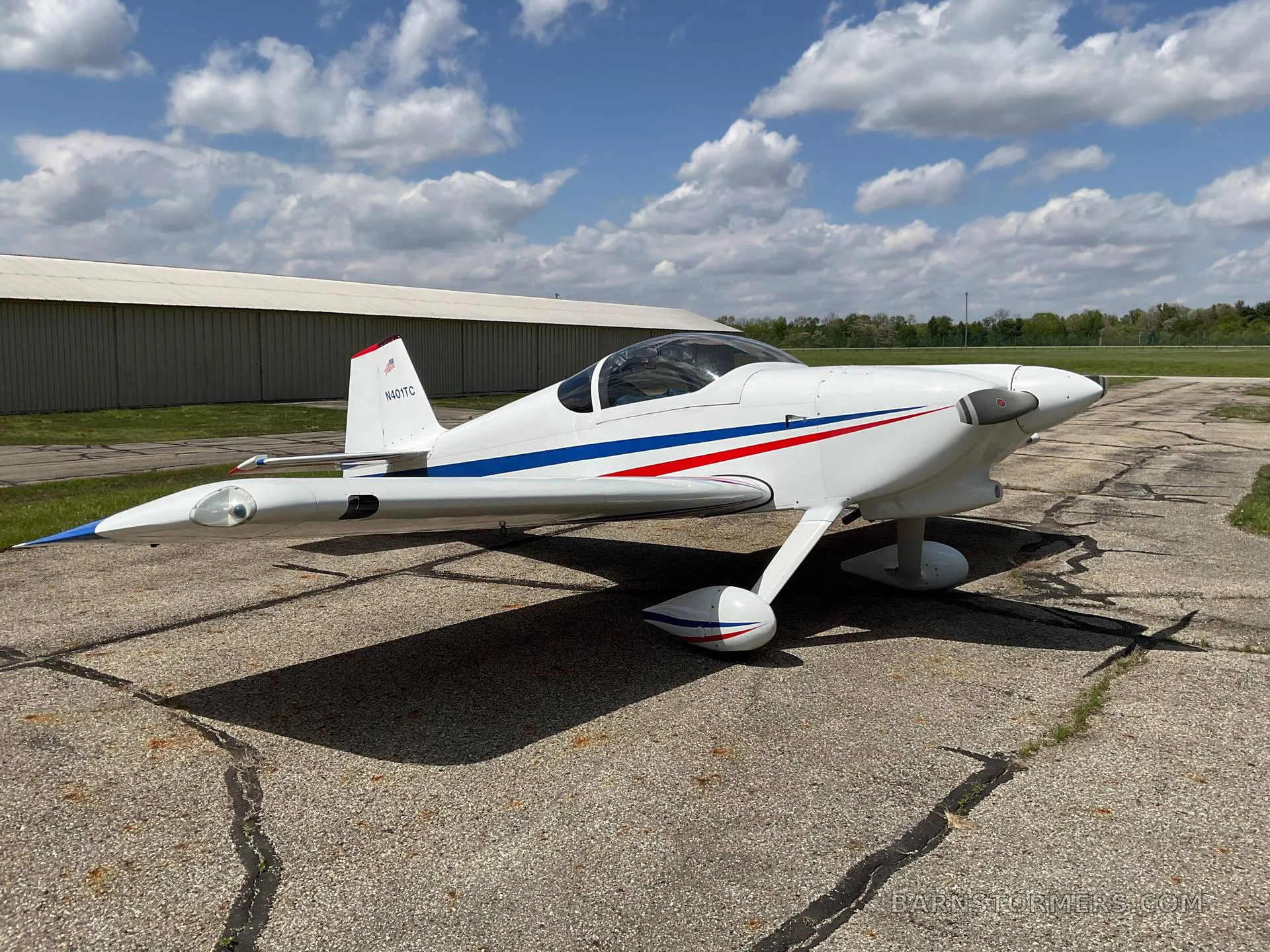 A white single-engine aircraft with a blue stripe (N401TC), parked on an asphalt tarmac under a partly cloudy sky.