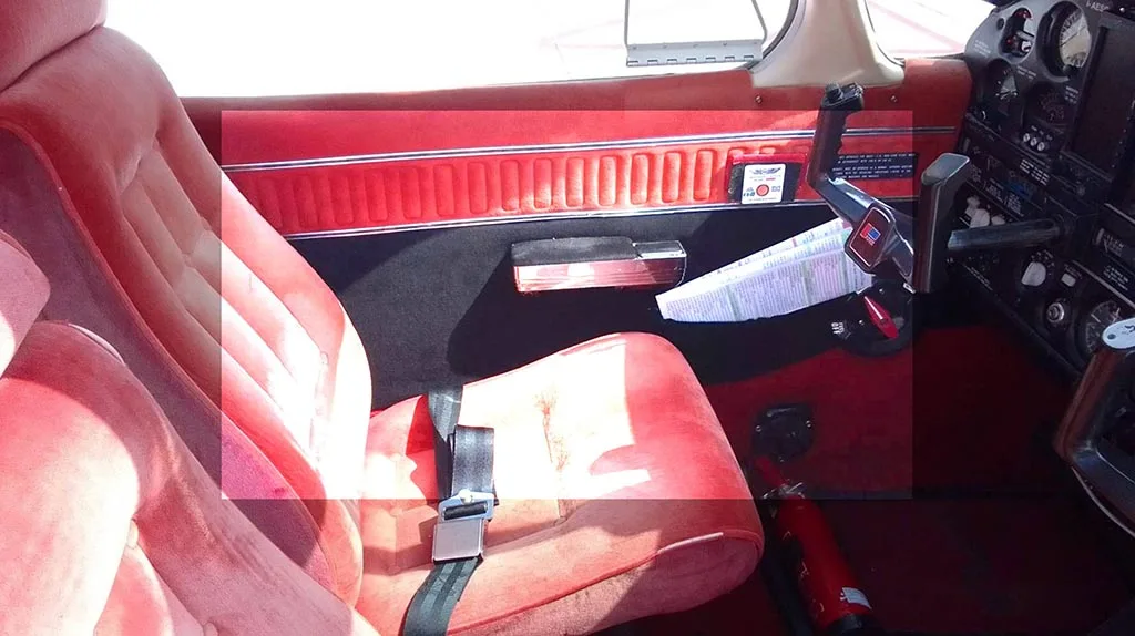 The red fabric pilot's seat and side panel of a small aircraft, showing part of the controls.