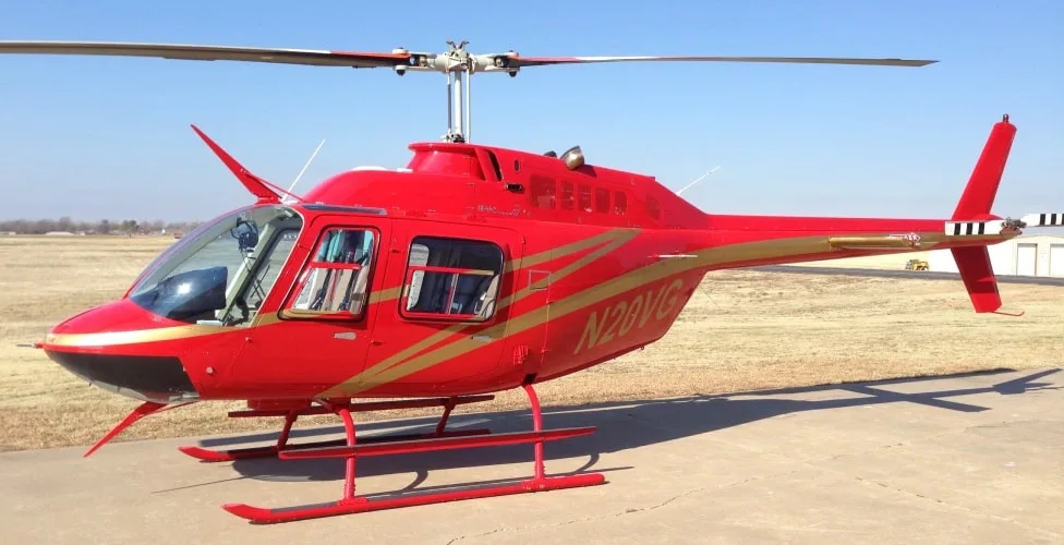A red helicopter with gold stripes and registration N20VG sits on a tarmac at an airfield under a clear blue sky.