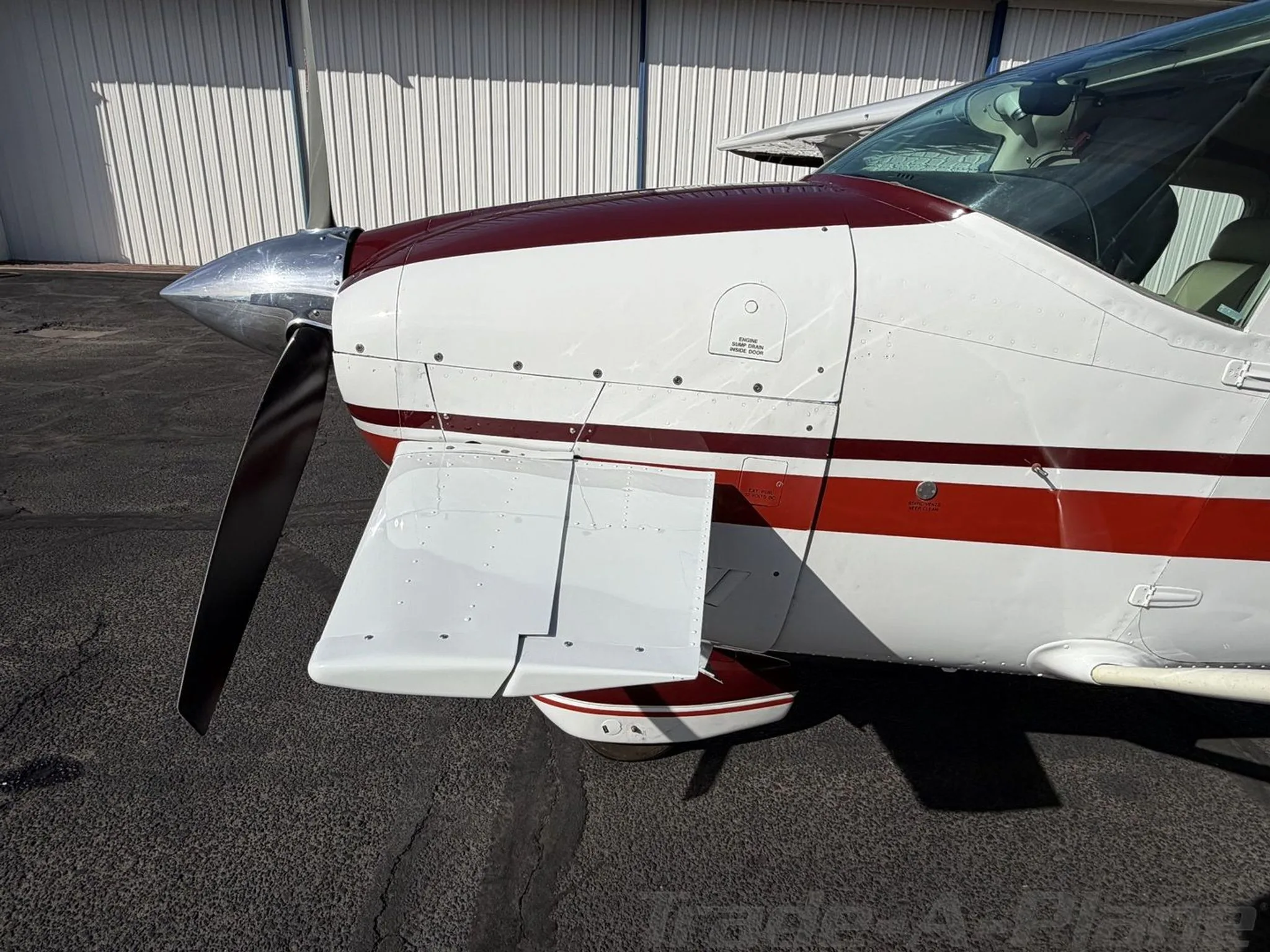 A close-up side view of the engine cowling and front landing gear of the white and red Cessna Skylane II.