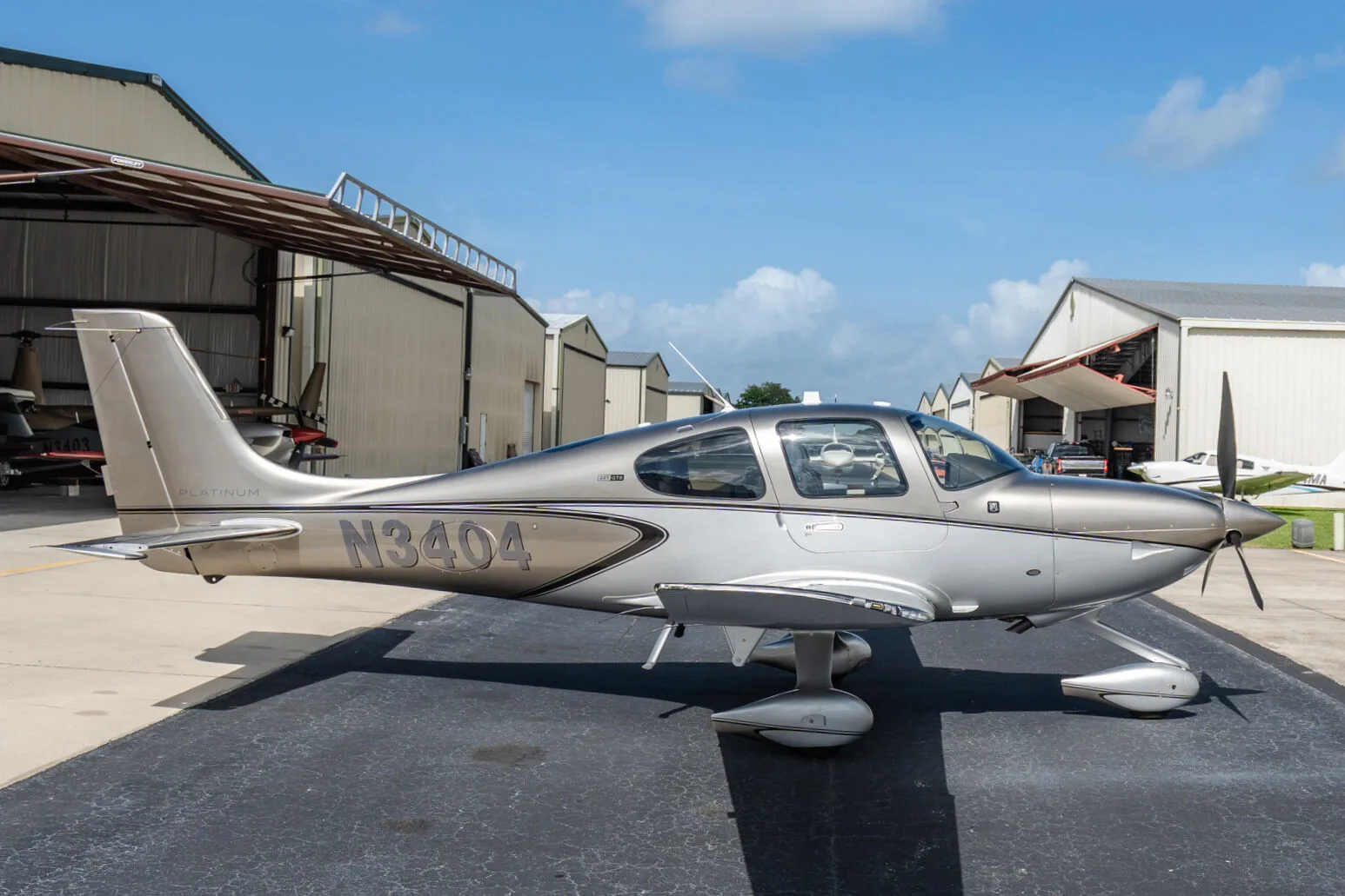 Side view of a silver Cirrus SR22T aircraft (N3404) parked on an airport tarmac under a blue sky.