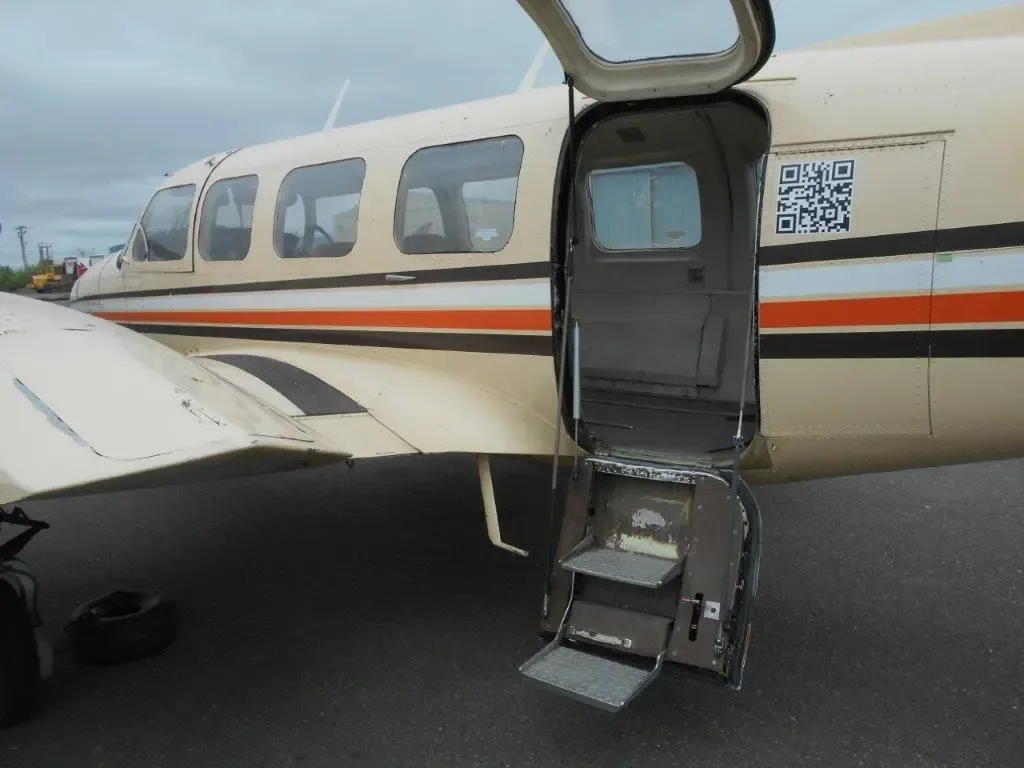 A side view of the beige Piper Navajo aircraft, N4112E, with its passenger door open, revealing built-in steps.
