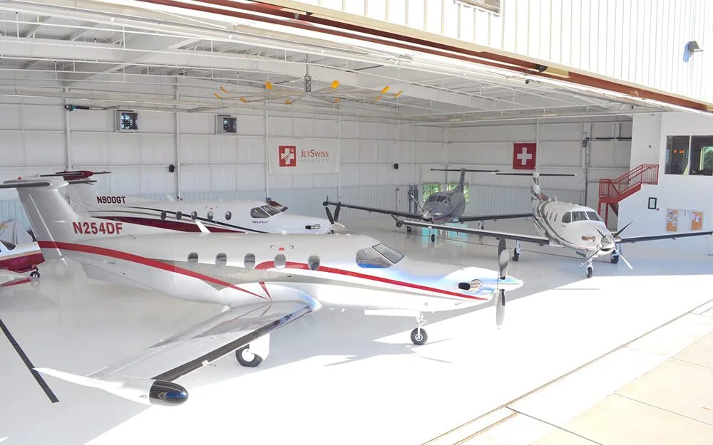 Three Pilatus PC-12 turboprops, one with red and white stripes and tail number N254DF, parked inside a bright white hangar.