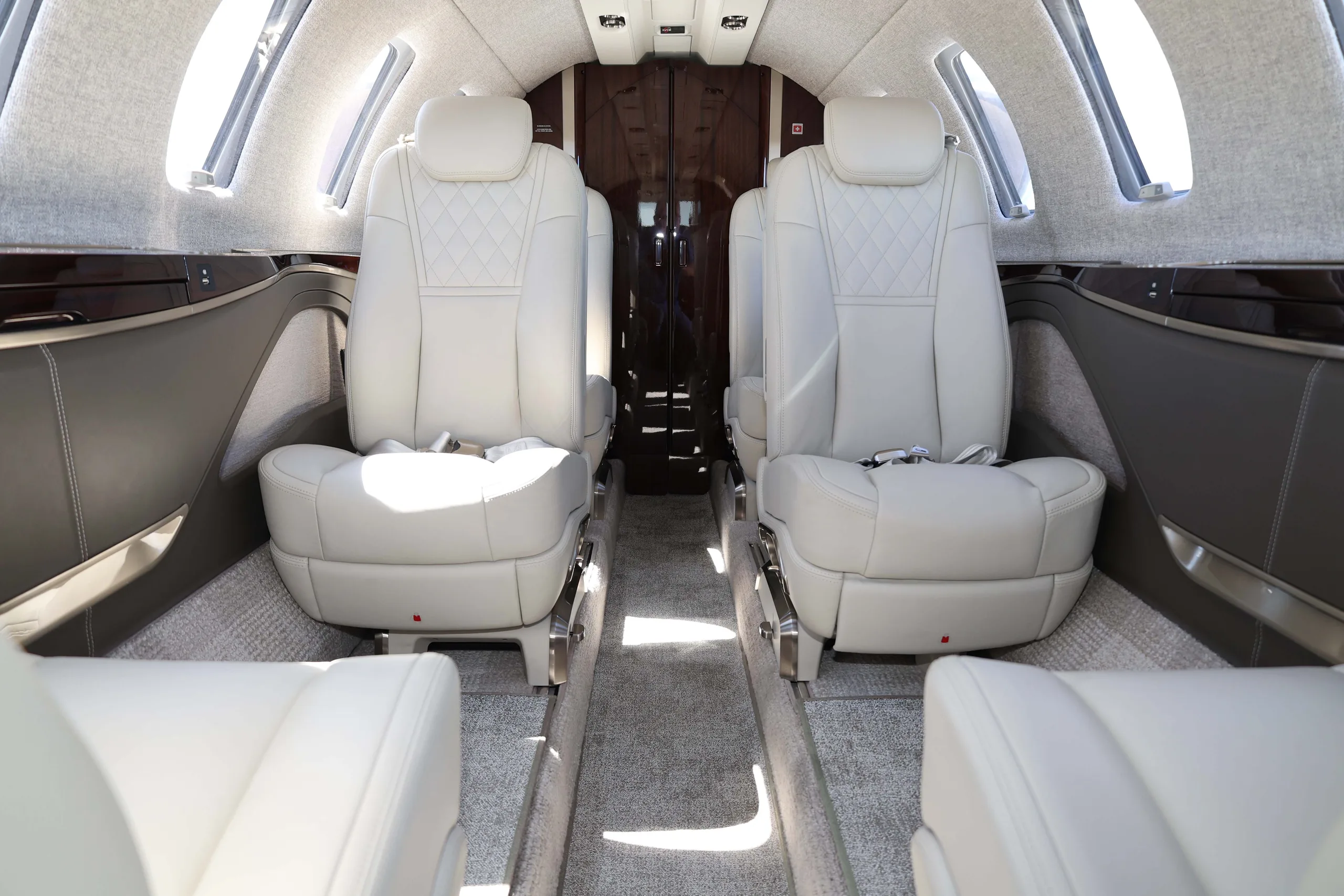 The interior cabin of a private jet, showing two rows of light-colored leather seats with quilted patterns.