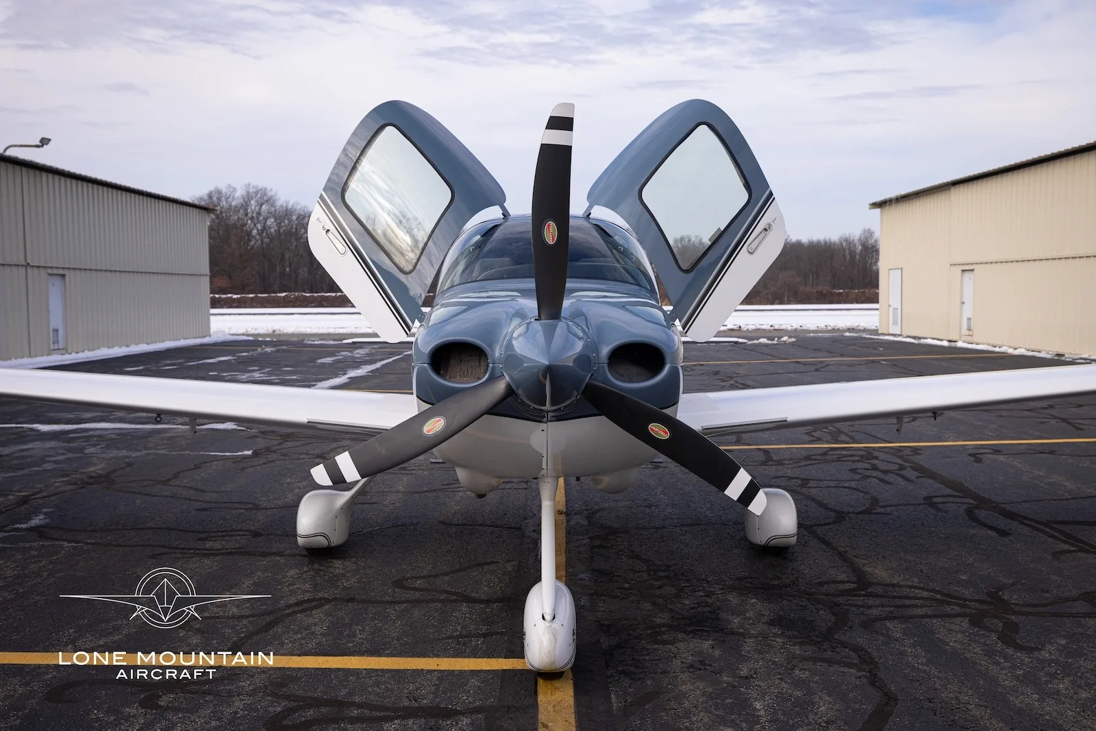 A front view of the Cirrus SR20 aircraft, N334MR, with its gull-wing doors open, parked on a tarmac.