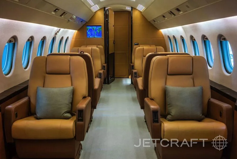 The interior cabin of a business jet with tan leather seats and a screen displaying a map.