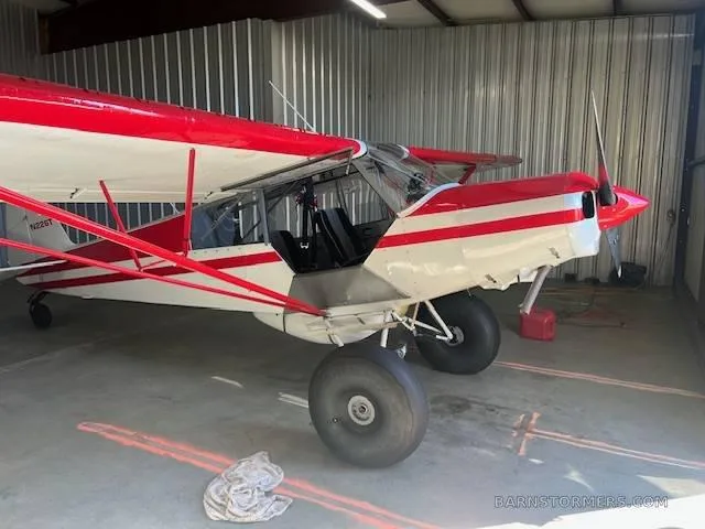 A red and white bush plane with large tires and an open door, tail number N226T, parked inside a metal hangar.