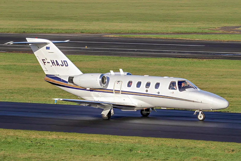A white business jet with blue and gold stripes, registration F-HAJD, taxiing on a runway.