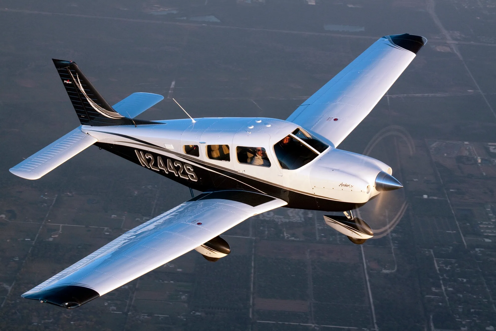 A white and black Piper Archer TX aircraft with registration N2442S is flying over a landscape, viewed from above.