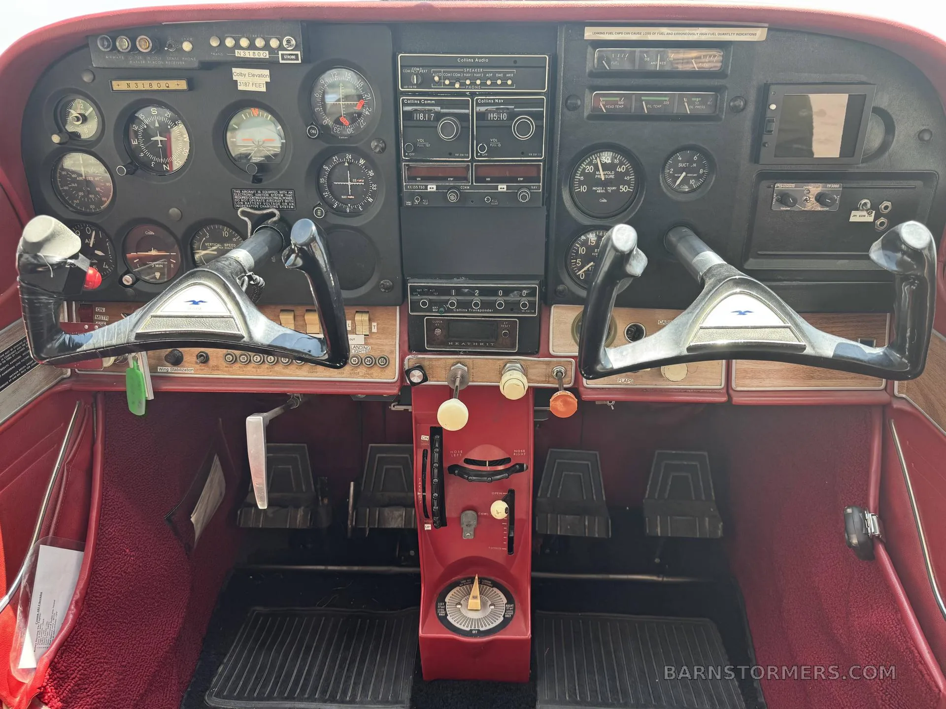 The cockpit of a small aircraft, featuring a dark instrument panel with analog gauges, radios, and two control yokes, with red carpeting.