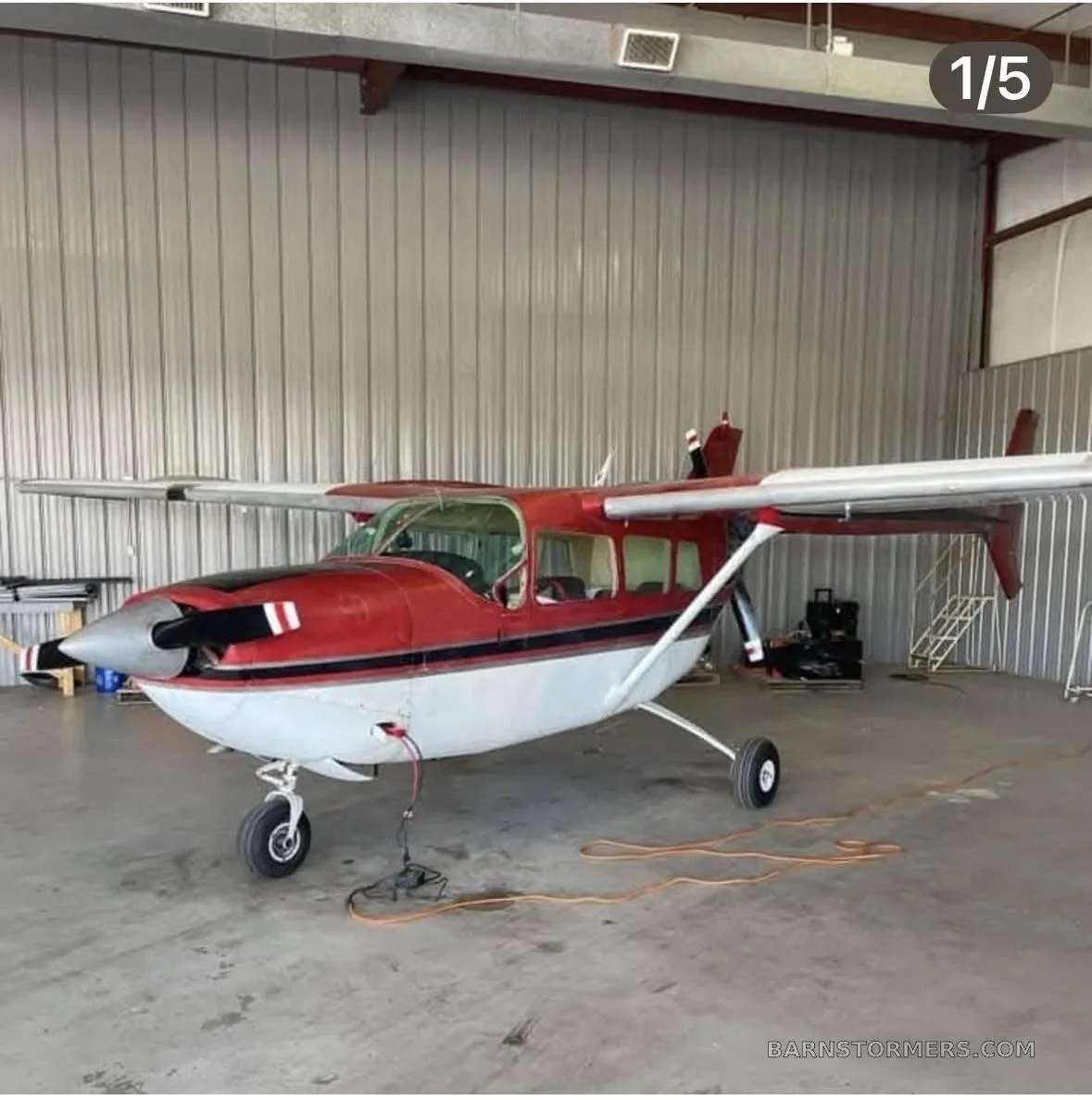 A red and white high-wing single-engine aircraft with a black propeller spinner, parked inside a hangar.