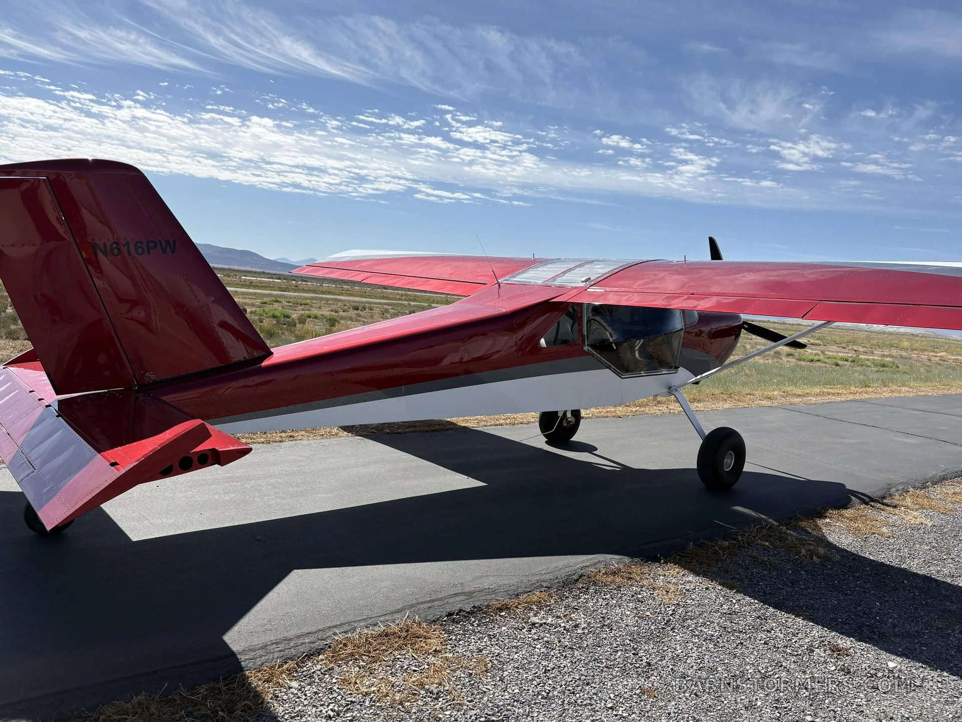 A rear-side view of a red and white single-engine aircraft with tail number N616PW on an asphalt strip.