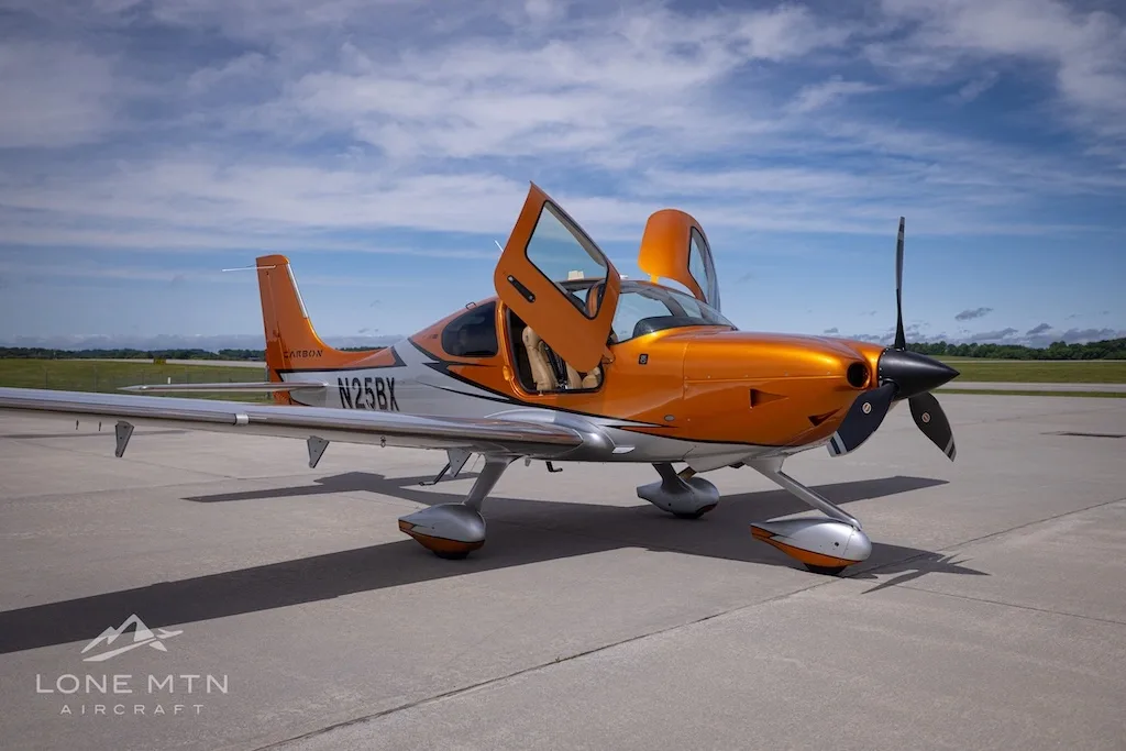 A front-right view of the orange and silver Cirrus SR22T N25BX with its doors open on an airfield.