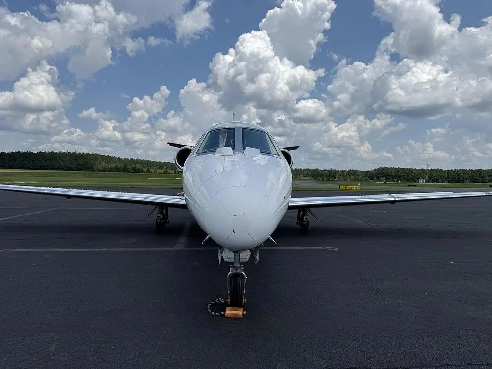A head-on view of a white Cessna Citation private jet with black and grey stripes parked on an airport tarmac.