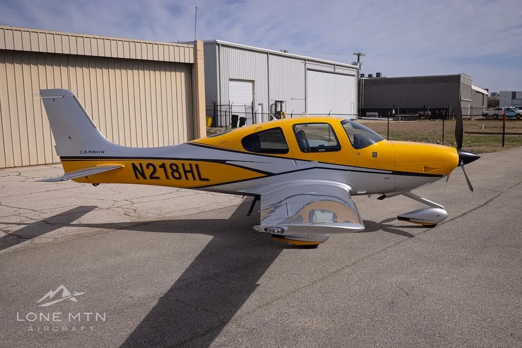 A Cirrus SR22 aircraft with yellow and silver paint scheme parked on an airfield, showing the right side.