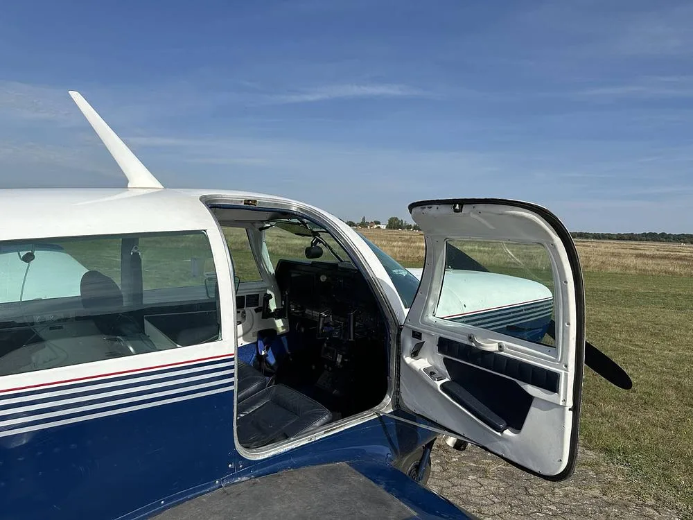 The open door of a blue and white aircraft reveals the dark blue interior seats and a glimpse of the cockpit.