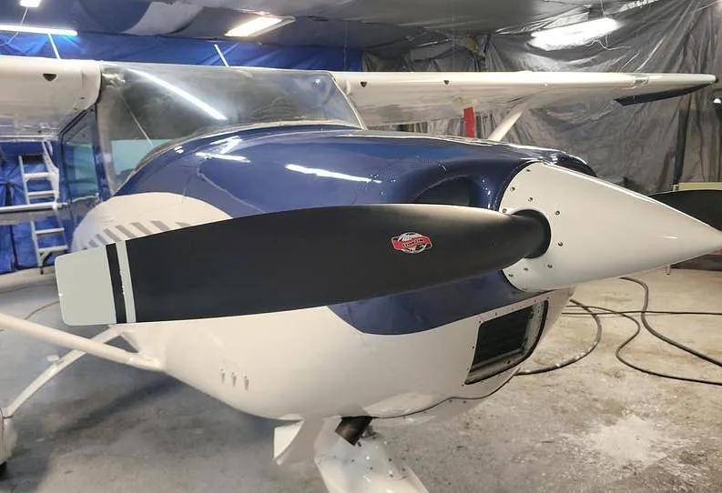 A front-quarter view of the blue and white Cessna N4303S's nose and propeller in a hangar.