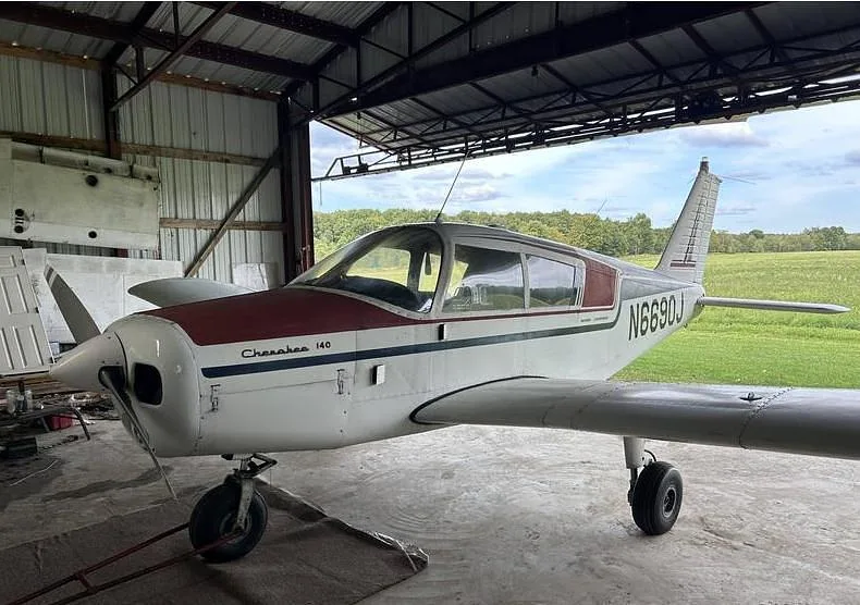 A white and maroon Piper Cherokee 140 aircraft, N6690J, parked inside a hangar with its nose facing left.