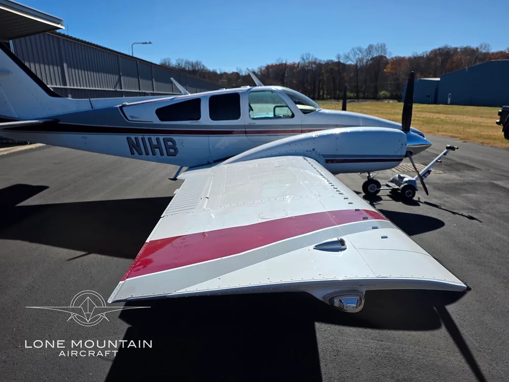 A close-up view of the wing and fuselage of the white and red twin-engine aircraft, N1HB, on an airfield.
