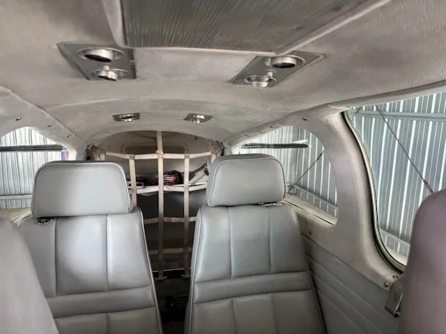 The grey leather interior cabin of an aircraft, showing two rows of seats and a cargo net in the rear.