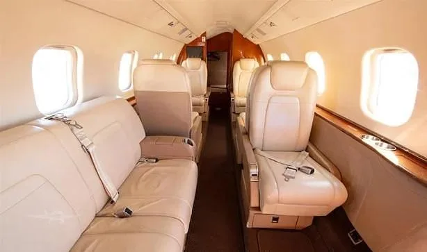 A view of the private jet's cabin, showing beige leather seating arrangements and a spacious aisle.