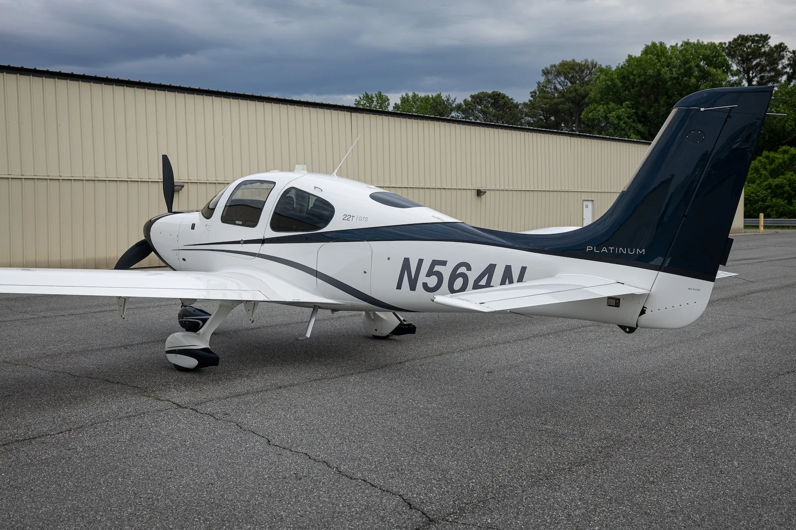 A white and dark blue Cirrus SR22T aircraft with registration N564N parked on an asphalt ramp, showing the tail and right side.