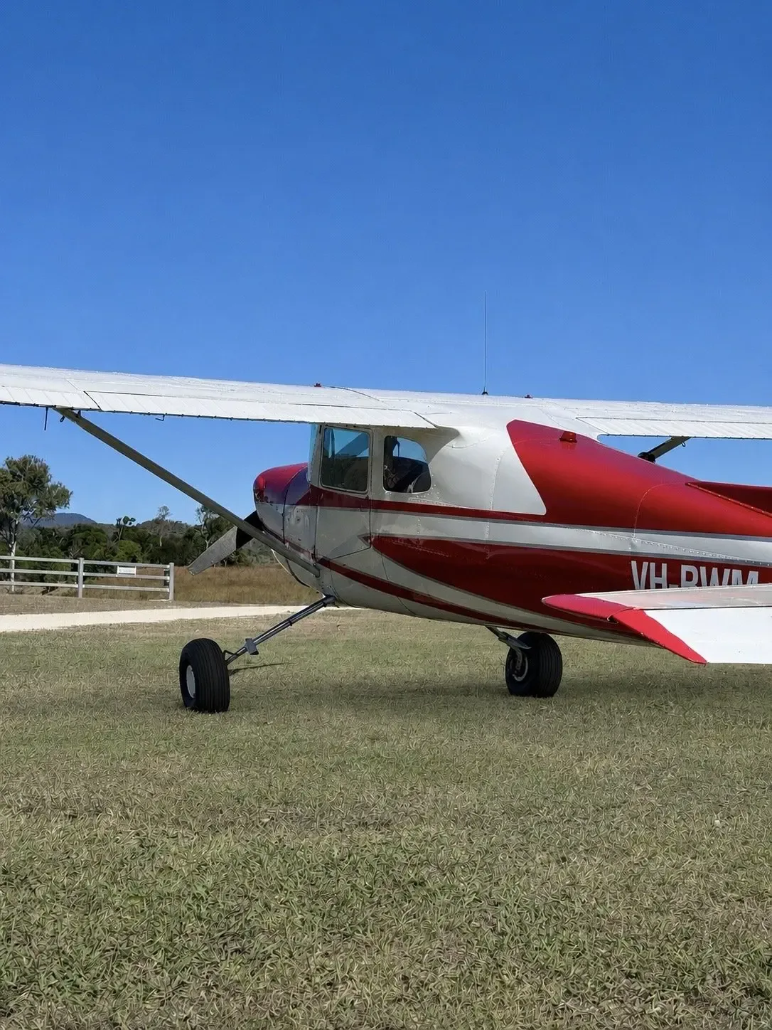 A side view of a red and white single-engine propeller aircraft, registration VH-RWM, on a grassy field.