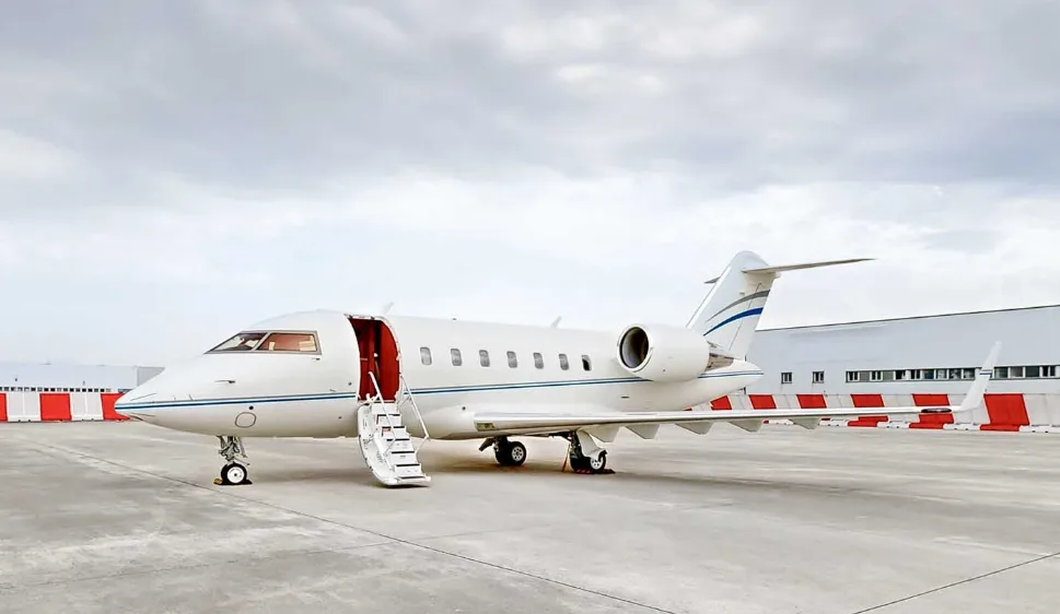 A white Bombardier Challenger business jet with blue accent stripes and an open entry door on a tarmac.